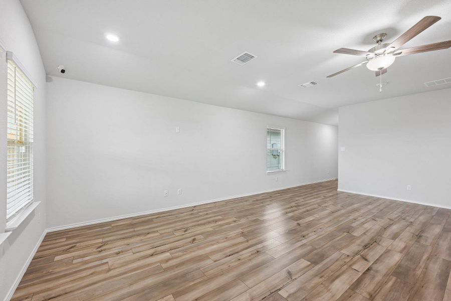 Spacious room featuring wood-finish flooring, white walls, recessed lighting, a ceiling fan with light fixture, and windows with blinds
