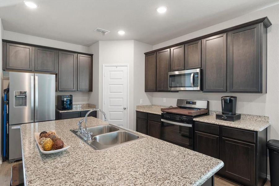 Kitchen with dark brown cabinetry, sink, an island with sink, appliances with stainless steel finishes, and light wood-type flooring