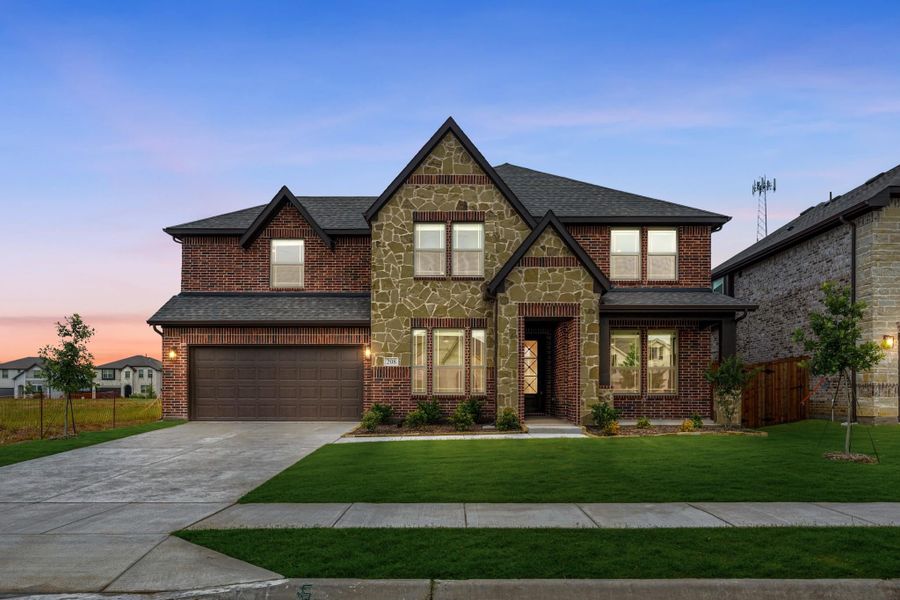 Two-story brick and stone home with two-car garage and front lawn at dusk Two-story brick and stone home with two-car garage and front lawn at dusk