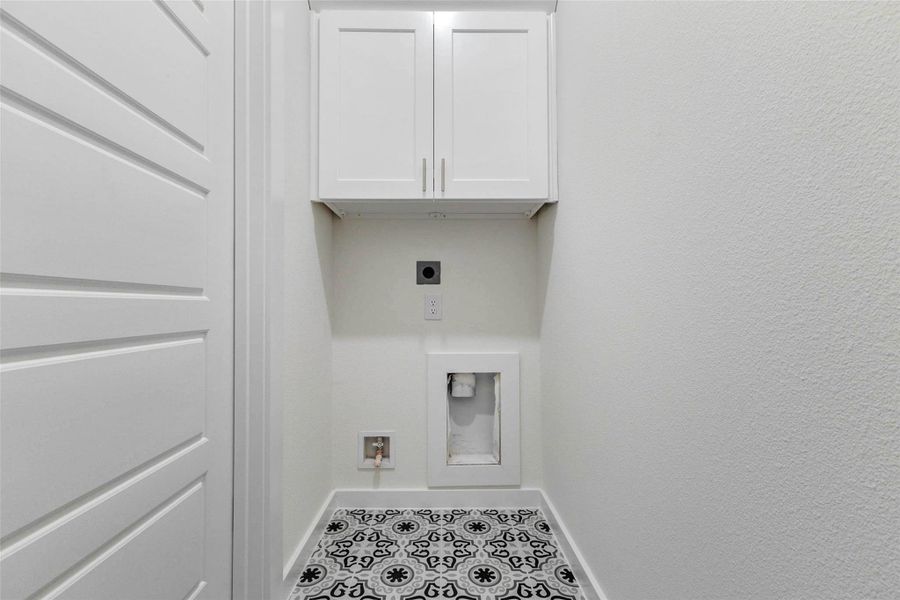 Convenient in-home utility space with washer and dryer connections, overhead storage cabinetry, patterned tile flooring, and a clean, tucked-away layout. This dedicated laundry area keeps everyday chores organized while offering useful cabinet storage for detergents, linens, or household supplies.