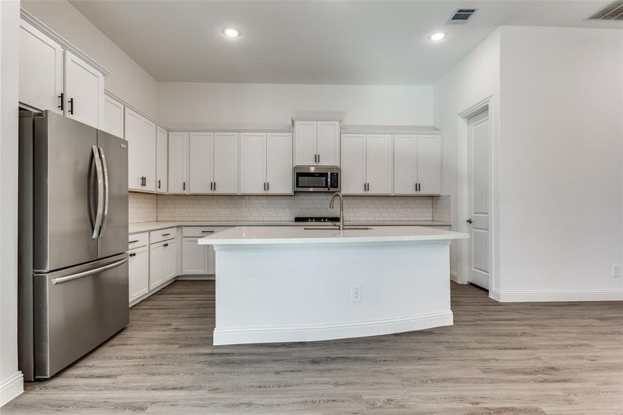 Kitchen with large center island sink, SS appliances with white cabinetry, and breakfast bar