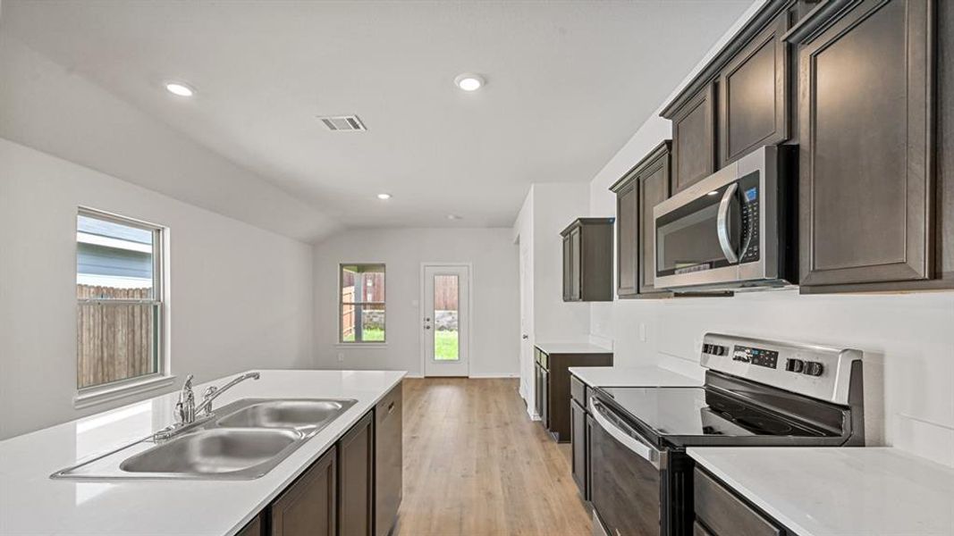 Modern kitchen featuring stainless steel appliances, dark wood cabinetry, and white countertops