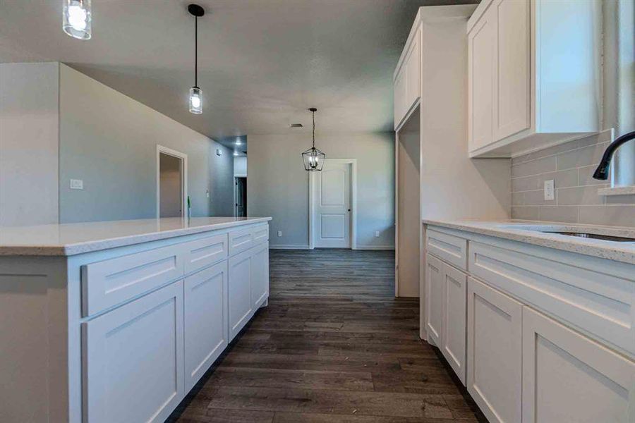 Kitchen featuring white cabinets, dark wood-type flooring, decorative light fixtures, and decorative backsplash Kitchen featuring white cabinets, dark wood-type flooring, decorative light fixtures, and decorative backsplash