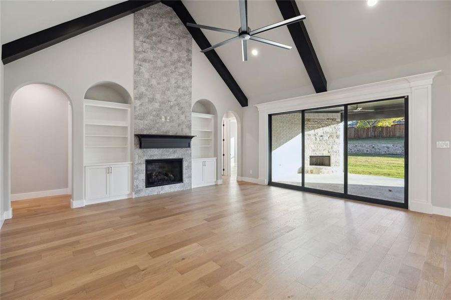 Unfurnished living room with built in shelves, a stone fireplace, light wood-type flooring, and high vaulted ceiling