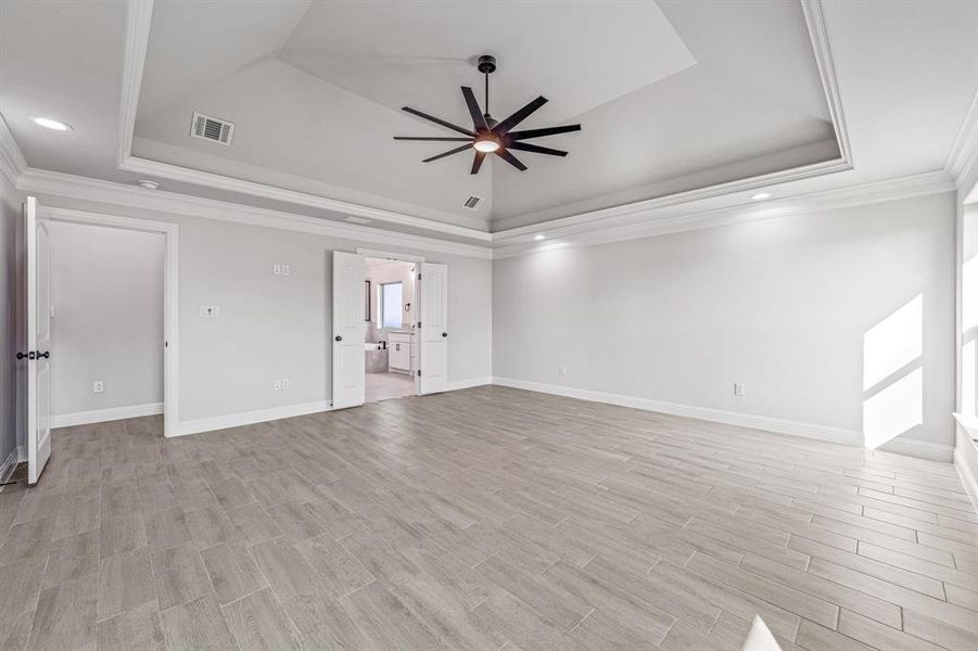 Unfurnished bedroom with a tray ceiling, crown molding, ceiling fan, wood tiled floors, and connected bathroom