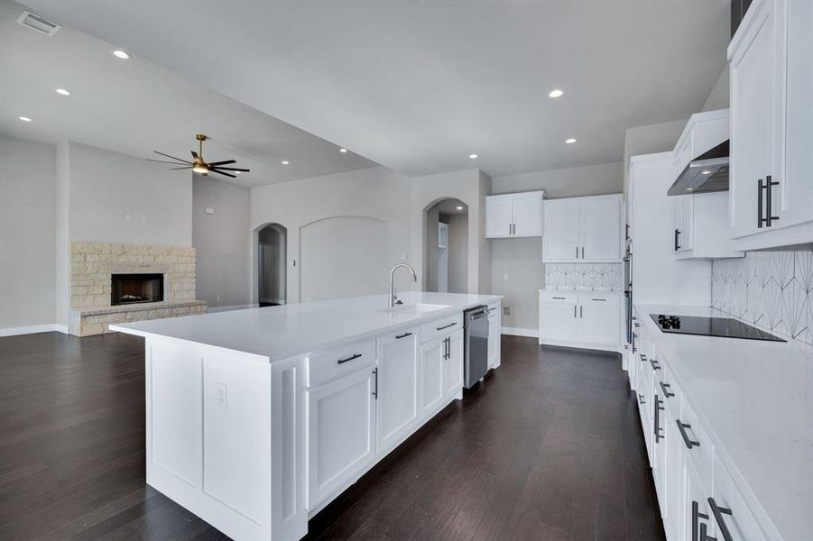 Kitchen with electric cooktop, a fireplace, dark wood-type flooring, and an island with sink