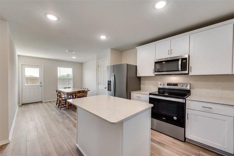 Kitchen with a kitchen island, LVP flooring, stainless steel appliances, white cabinets, and a kitchen bar