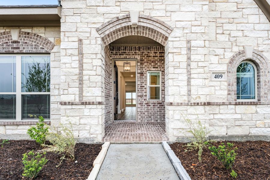 Home entrance with arched brick doorway, stone exterior, and concrete walkway leading to open front door