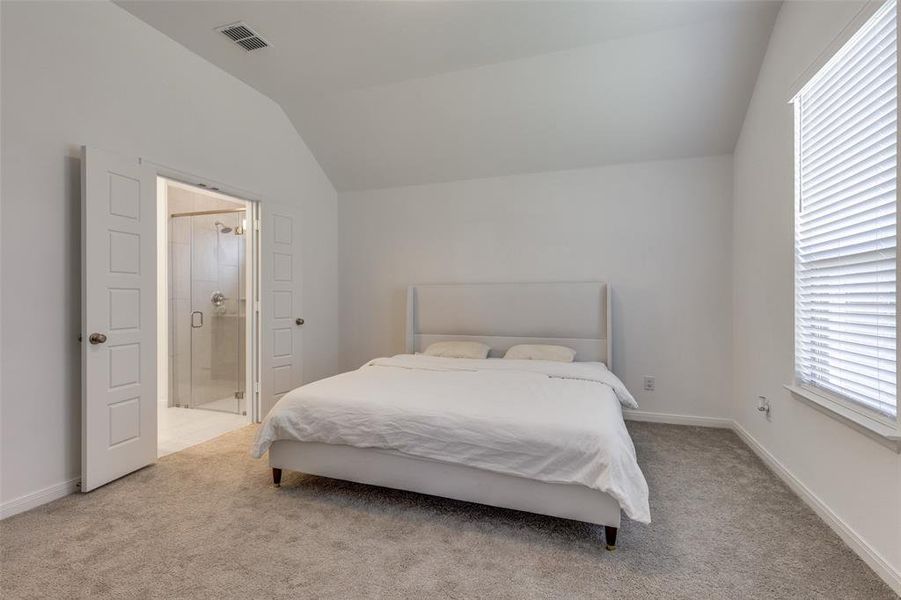Bedroom featuring vaulted ceiling, light colored carpet, and ensuite bath