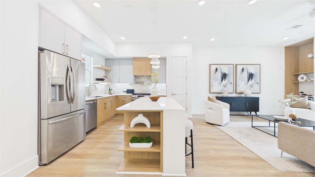 This photo showcases a modern, open-concept kitchen and living area. The kitchen features stainless steel appliances, light wood cabinets, and a central island with bar seating. The living space is bright and airy, with contemporary furnishings and decor.