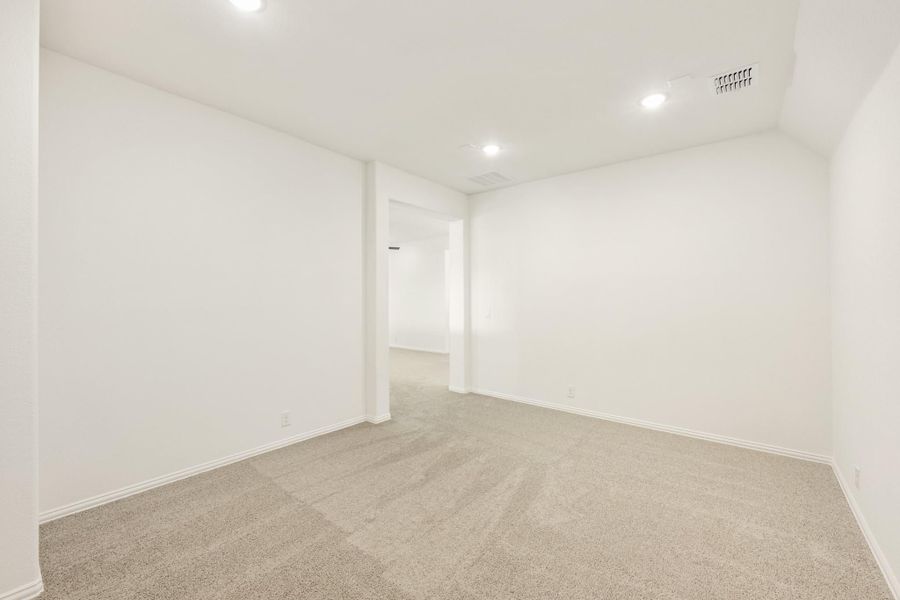 Empty bedroom with beige carpet, white walls, recessed lighting, and open doorway to hallway