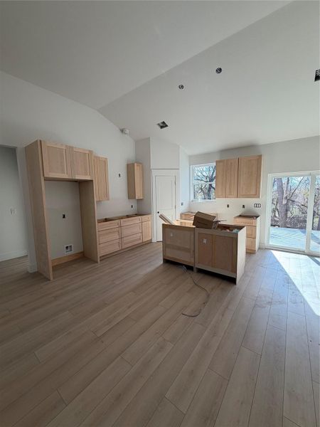 Kitchen with light brown cabinets, a kitchen island, vaulted ceiling, and light wood-type flooring