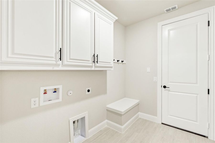 Laundry room with white upper cabinets, washer and dryer hookups, wall hooks, and a built-in bench Laundry room with white upper cabinets, washer and dryer hookups, wall hooks, and a built-in bench