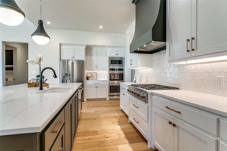 Kitchen featuring light stone countertops, wall chimney exhaust hood, backsplash, white cabinets, and light wood-style floors