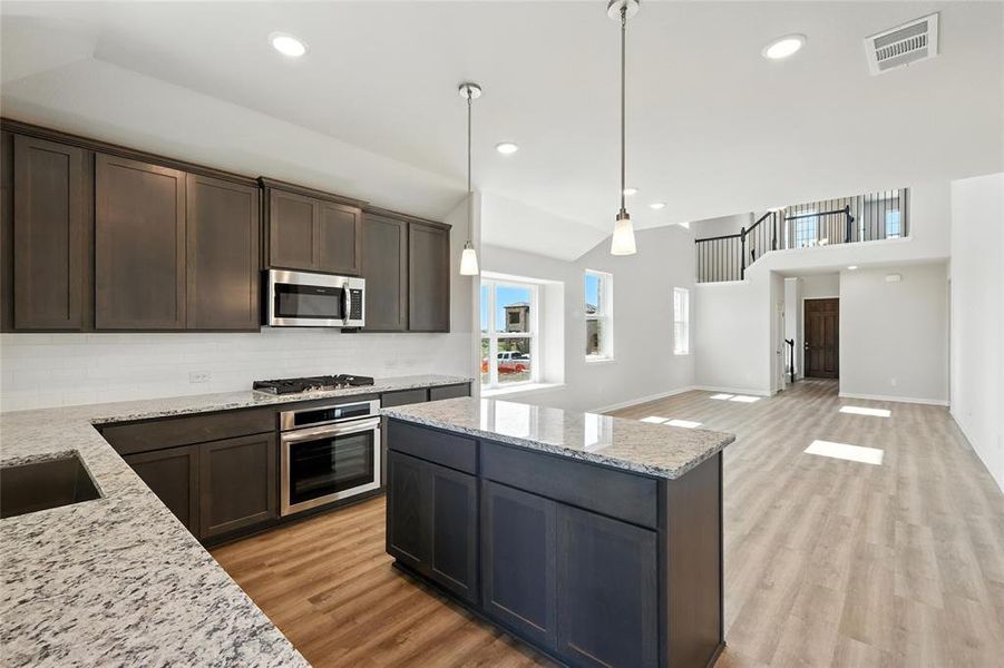 Kitchen featuring appliances with stainless steel finishes, dark brown cabinetry, light wood-type flooring, tasteful backsplash, and decorative light fixtures Kitchen featuring appliances with stainless steel finishes, dark brown cabinetry, light wood-type flooring, tasteful backsplash, and decorative light fixtures