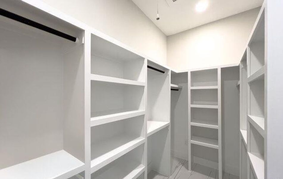 Expansive custom closet featuring extensive built-in shelving, multiple hanging rods, recessed lighting, and light-toned flooring