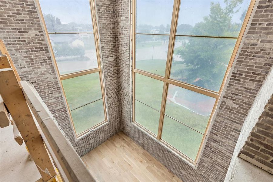 Double-height space featuring extensive window walls with wood-finish framing, light wood-finish flooring, and exposed gray brick interior walls
