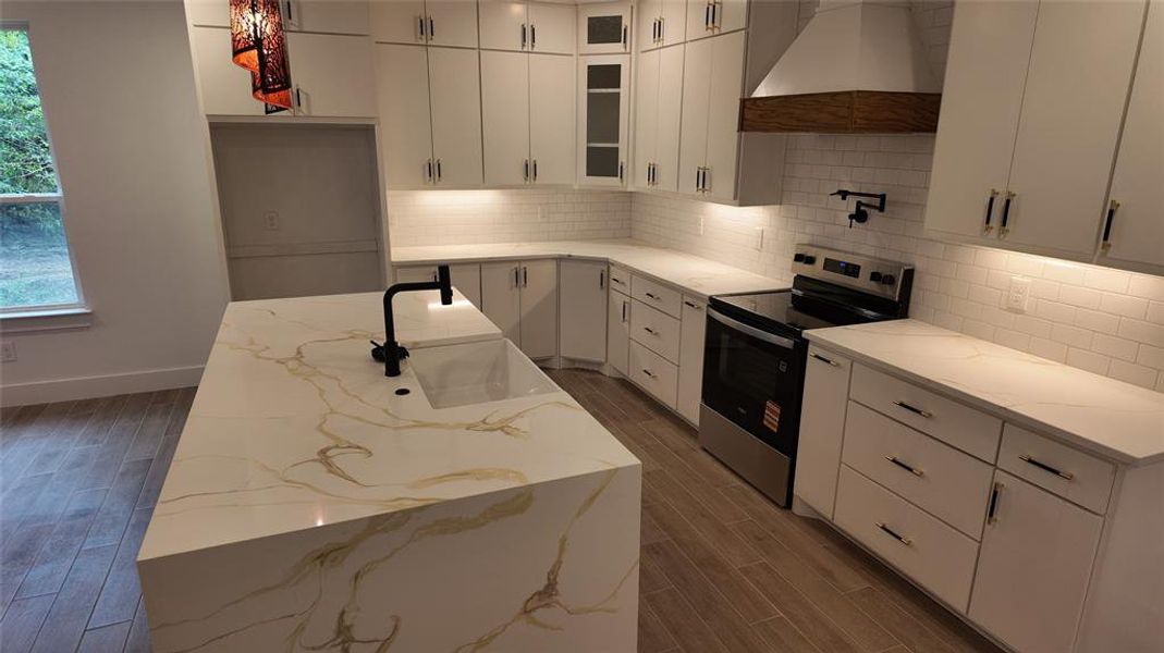 Kitchen with electric range, light stone countertops, and custom exhaust hood Kitchen with electric range, light stone countertops, and custom exhaust hood
