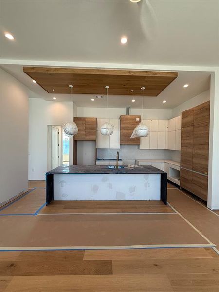 Kitchen with modern cabinets, wood finished floors, a center island with sink, recessed lighting, and dark stone countertops