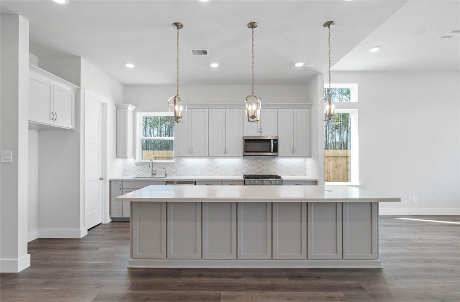 The kitchen anchors the space with gorgeously stained wood cabinetry, stainless steel appliances, sleek white quartz countertops, and a large island perfect for casual dining or hosting.