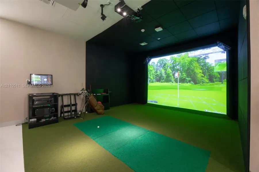 Golf simulator room featuring a large-scale projection screen, synthetic turf flooring, sound-dampening wall panels, and ceiling-mounted projection hardware
