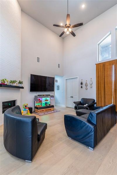Living area featuring light wood-style floors, a towering ceiling, and ceiling fan
