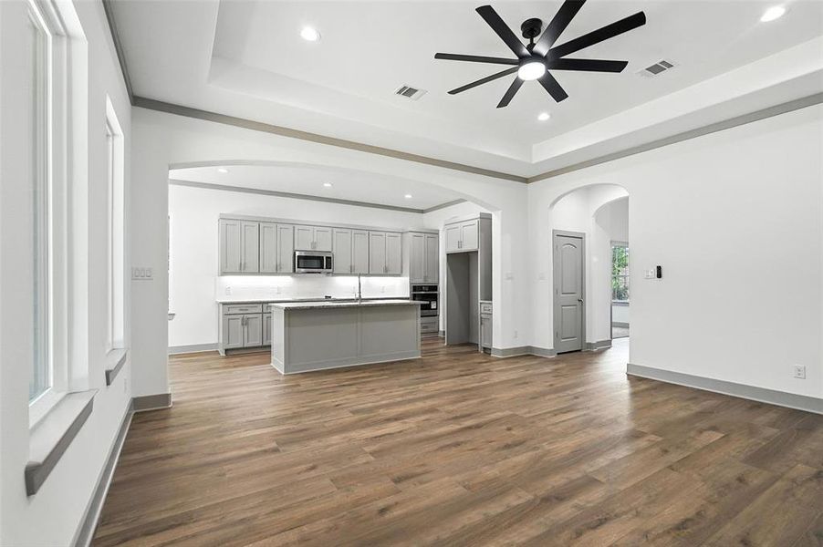 Unfurnished living room featuring arched walkways, a raised ceiling, recessed lighting, dark wood-style flooring, and a ceiling fan Unfurnished living room featuring arched walkways, a raised ceiling, recessed lighting, dark wood-style flooring, and a ceiling fan