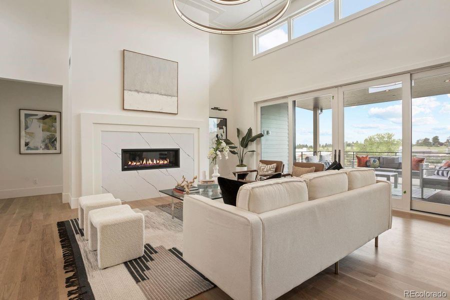 The great room features a sleek linear fireplace framed in marble-inspired tile, soaring ceilings, and expansive glass doors opening to the outdoor living area.
