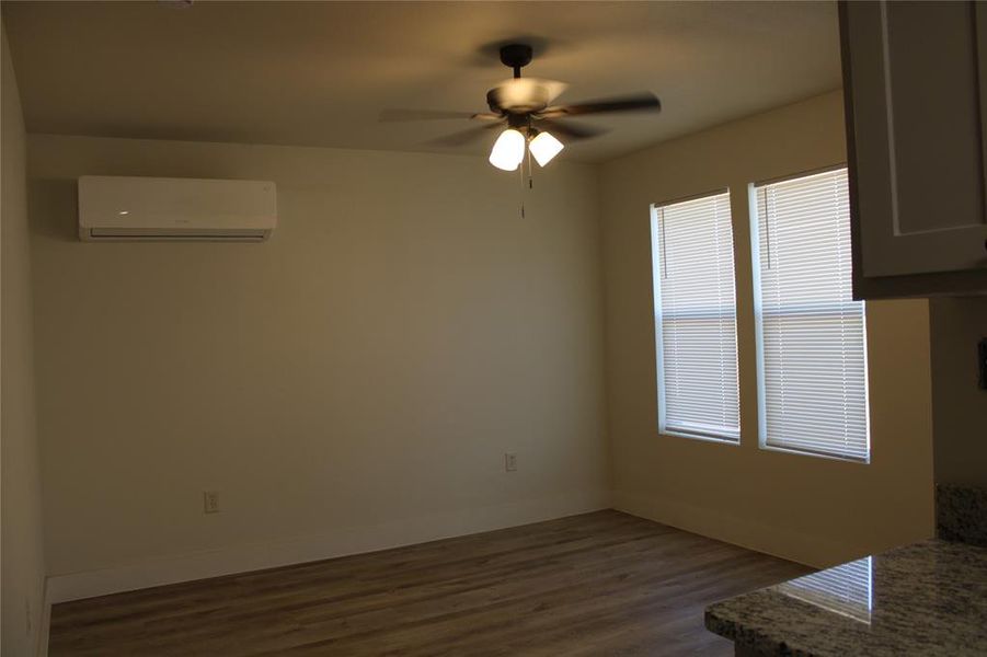 Unfurnished dining area with dark wood-style floors, ceiling fan, and a wall mounted air conditioner