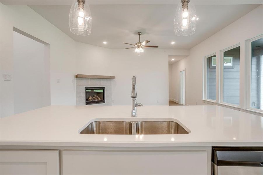 Kitchen featuring ceiling fan, a tiled fireplace, decorative light fixtures, sink, and white cabinetry