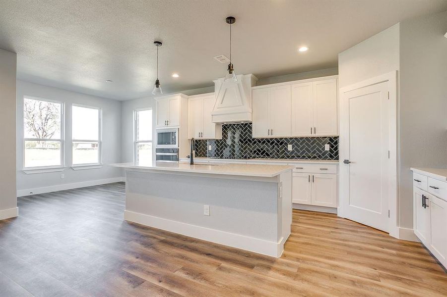 Kitchen with backsplash, decorative light fixtures, white cabinets, an island with sink, and recessed lighting