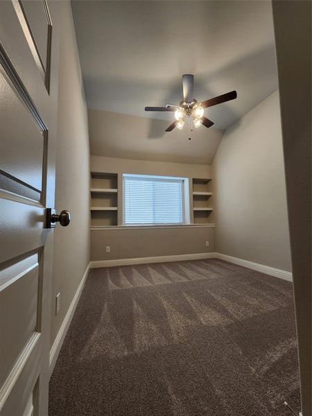 Empty room with ceiling fan, carpet, vaulted ceiling, and built in shelves