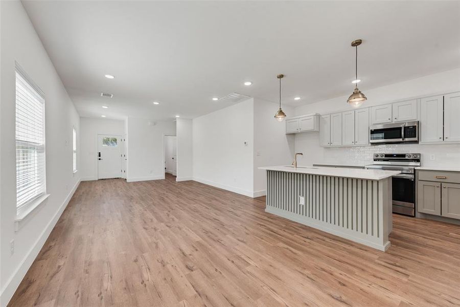 Kitchen featuring stainless steel appliances, decorative light fixtures, gray cabinets, backsplash, and an island with sink Kitchen featuring stainless steel appliances, decorative light fixtures, gray cabinets, backsplash, and an island with sink
