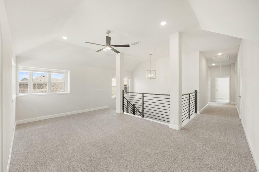 Open upstairs loft with vaulted ceiling, ceiling fan, carpet floors, and metal stair railing overlooking lower level