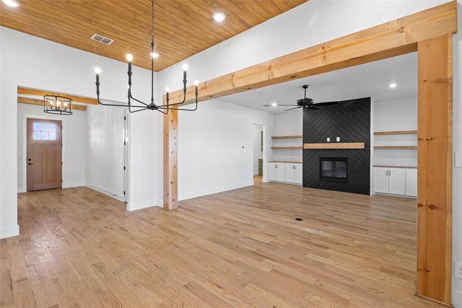 Unfurnished living room with ceiling fan with notable chandelier, wood ceiling, a fireplace, and light hardwood / wood-style flooring