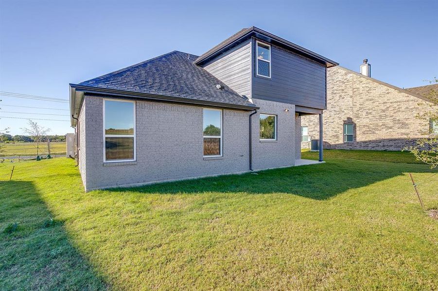 Rear view of property with brick siding, a yard, a patio area, a shingled roof, and a chimney
