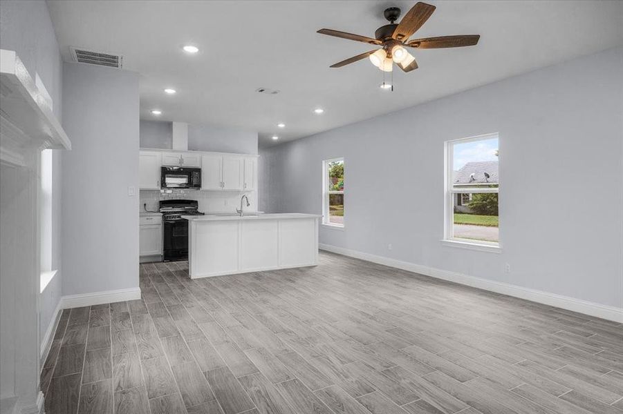 Kitchen with black appliances, light wood finished floors, open floor plan, a ceiling fan, and light countertops