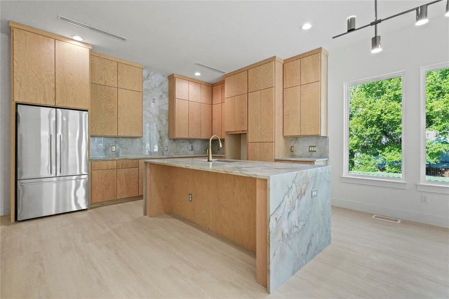 Kitchen with backsplash, freestanding refrigerator, light stone countertops, light wood finished floors, and decorative light fixtures