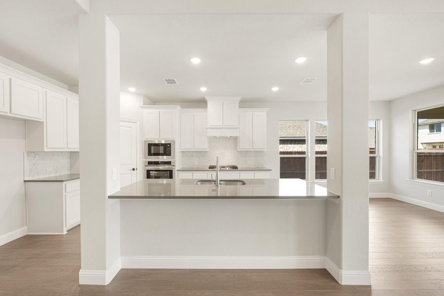 Open kitchen with white cabinets, gray island with sink, stainless steel appliances, and hardwood floors