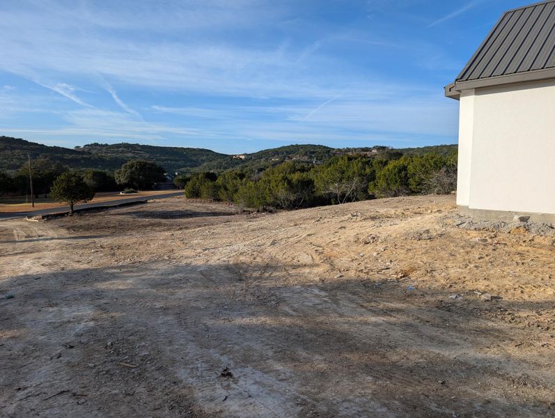 Expansive undeveloped land featuring a partial structure with a metal roof, scattered trees, and distant rolling hills