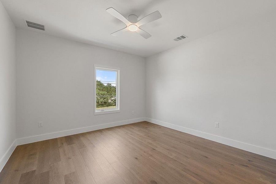 An inviting room features light hardwood flooring, clean white walls, and a modern ceiling fan.