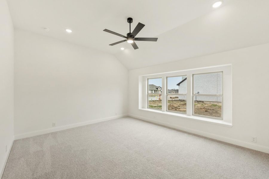 Empty bedroom with vaulted ceiling, ceiling fan, carpet flooring, and large triple window