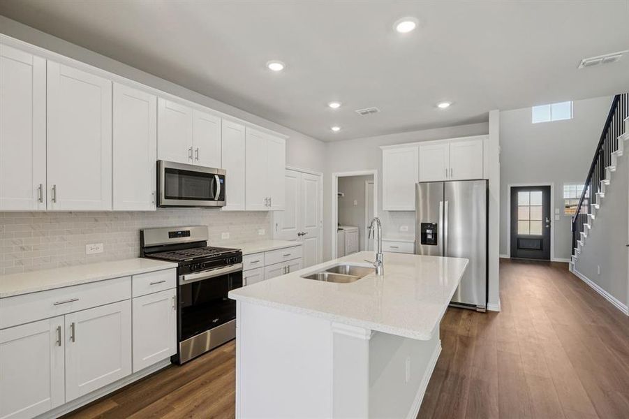 Kitchen featuring appliances with stainless steel finishes, white cabinets, an island with sink, recessed lighting, and light stone countertops