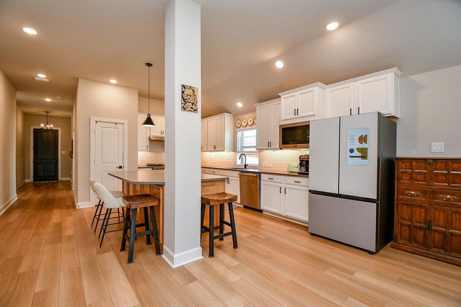 This modern kitchen features sleek white cabinetry, stainless steel appliances, and a stylish breakfast bar with seating. The open layout and wood flooring create a warm, inviting space perfect for cooking and entertaining.