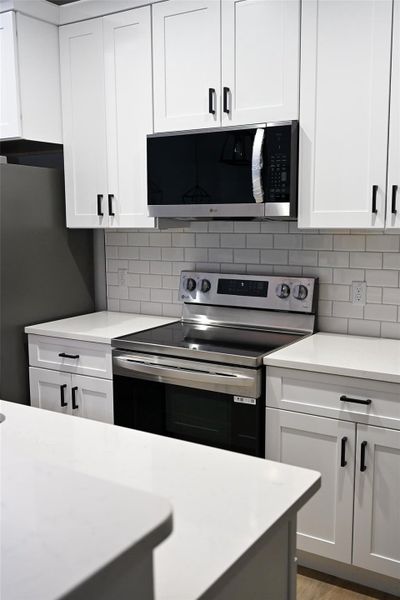 Kitchen with stainless steel appliances, white cabinets, light stone countertops, and tasteful backsplash