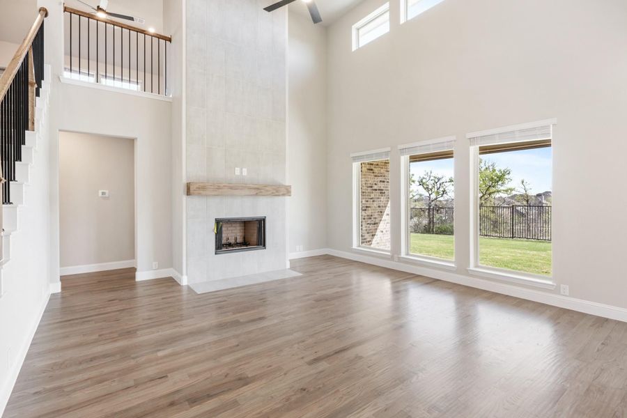 Open living room with two-story ceiling, tile fireplace, wood floors, and large windows overlooking backyard