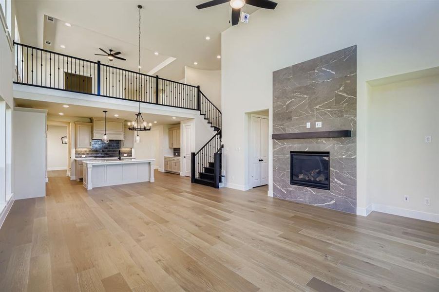 Unfurnished living room featuring a fireplace, ceiling fan, a towering ceiling, light wood-style flooring, and stairway