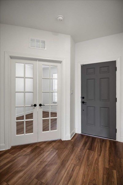 Rich wood flooring grounds this inviting entryway, featuring both a solid paneled door and elegant French doors.