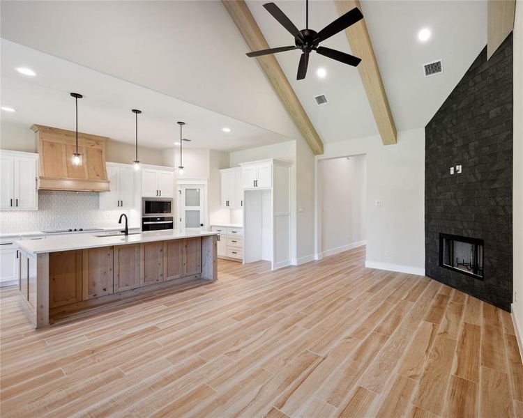 Kitchen with white cabinets, pendant lighting, light wood-type flooring, and a large island with sink