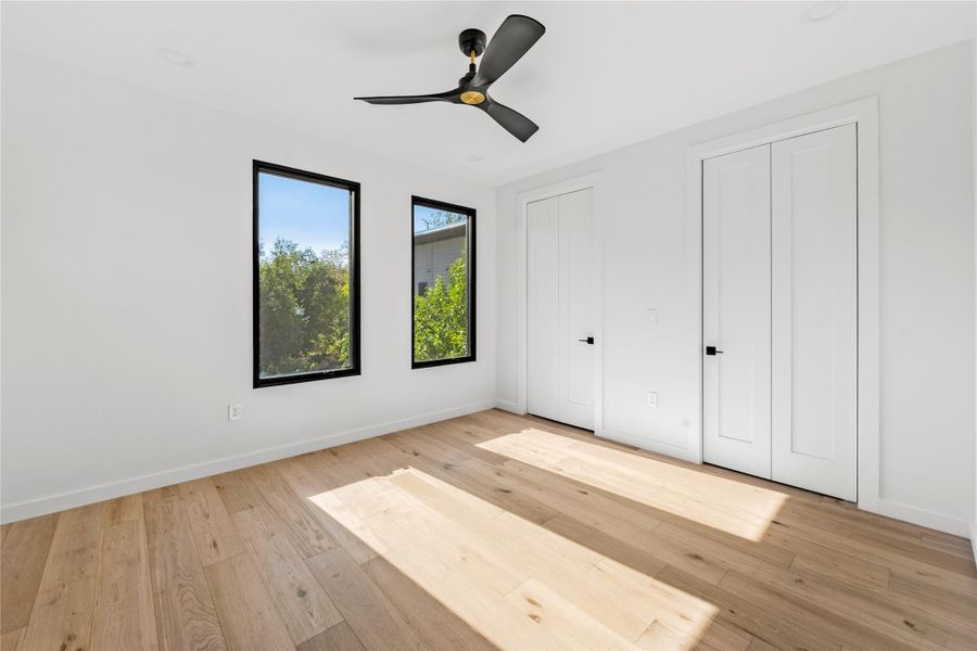 Unfurnished bedroom featuring multiple closets, light wood finished floors, and a ceiling fan
